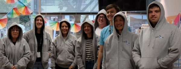A group of people in an office kitchen standing with their hoodies up.