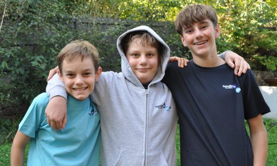 Three boys with arms around shoulders one in the middle with a hoodie up